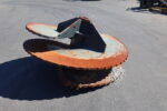 Two large rusted steel trencher discs with jagged teeth stacked on an asphalt surface.