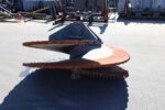 Rusty spiral auger conveyor in the foreground with blue metal housing, set in an outdoor industrial yard with equipment in the background.