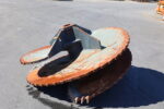 Close-up of a large, rusty circular cutting wheel with blue metal frame outdoors on asphalt.