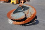 Large rusted circular saw blade on a construction site with forklift and orange cones in the background.