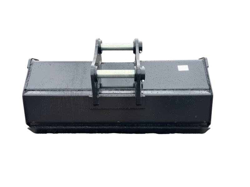 Heavy-duty black steel skid-steer bucket attachment with a mounting frame on top, sitting on a wet asphalt surface.