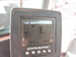 Close-up of a Dynapac digital instrument panel on a dusty surface, showing gauge bars and numeric readouts such as hours and percentages