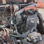 Diesel engine bay with blue and orange coolant hoses, wiring harnesses, and a cooling fan in the background.