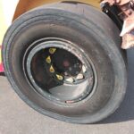 Close-up of a bus wheel: black tire on a metal rim with yellow lug nut covers and some rust/dirt.