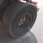 Close-up of a heavy-duty black tire mounted on a wheel with yellow lug nut caps, on a paved surface.