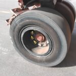 Close-up of a large aircraft wheel and tire on a tarmac, showing a rusted hub and brake components.