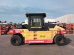 Yellow Dynapac CP224 road roller parked on asphalt in an industrial yard, with stacked equipment in the background.