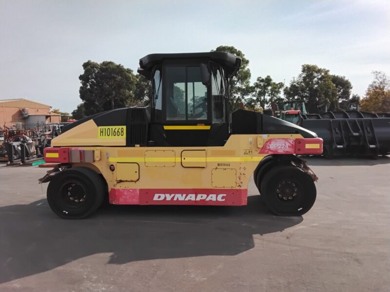 A Dynapac road roller with a yellow body and red base parked on a paved lot, single large front drum and an enclosed cab for the operator.