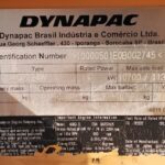 Close-up Dynapac nameplate showing model, specs, and identification number on orange equipment surface.