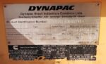 Close-up Dynapac nameplate showing model, specs, and identification number on orange equipment surface.