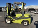 Green and black forklift parked in an outdoor industrial yard on a sunny day.