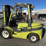 Green and black forklift parked in an outdoor industrial yard on a sunny day.
