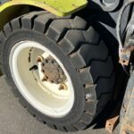 Close-up of a heavy equipment tire with a white rim and rusted lug nuts on a lime-green machine edge in view.