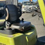 Green forklift with black driver seat and yellow safety frame in an outdoor yard.