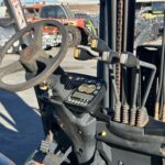 Close-up of a forklift cockpit showing steering wheel, multiple control levers, pedals, and a digital/ analog instrument panel