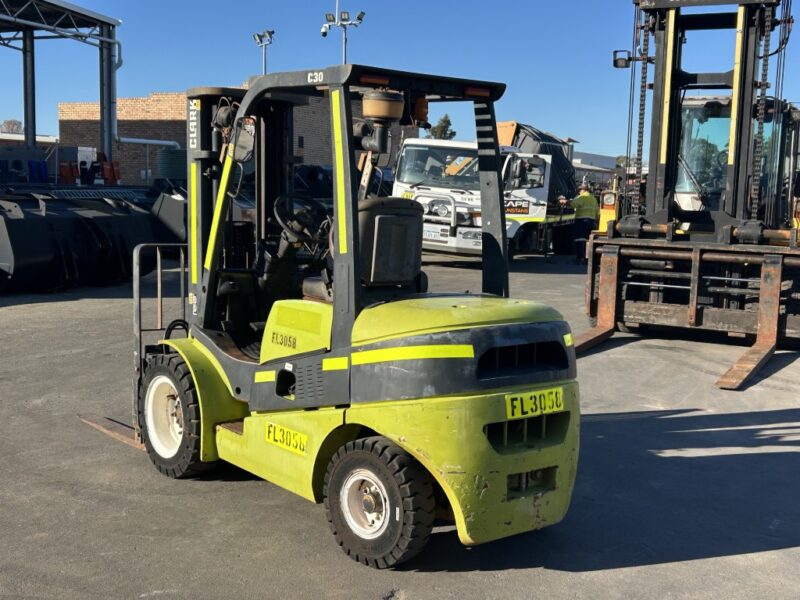 Green forklift with yellow stripes parked in an outdoor industrial yard with other heavy equipment in the background.