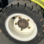 Close-up of a large forklift tire on a white steel rim with five rusted lug nuts and a yellow fender nearby.