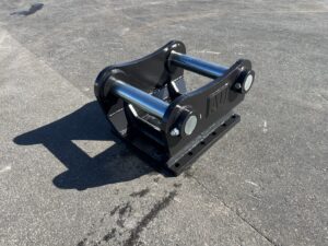 Heavy industrial quick-attach coupler for a skid-steer loader with blue pins and a black mounting plate on asphalt.